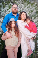Fototapeta premium Family allergic enjoying after treatment from seasonal allergy at spring. Happy mother, father and two daughters smiling in front of blossom tree at springtime. Spring allergy concept.