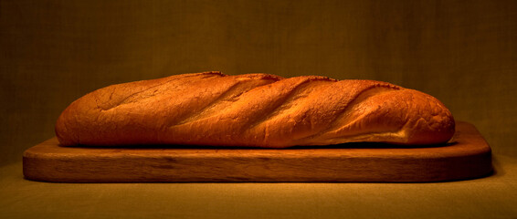 Low key digital photo of a French baguette bread with crispy crust on a wooden cutting board taken...
