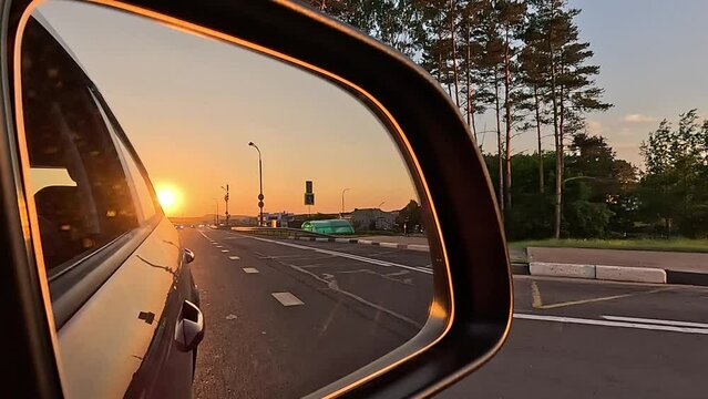 The sun is reflected in the mirror, evening road. View in the side rear view mirror of a red car driving along the highway