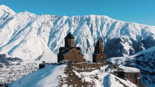 Ancient Christian monastery hidden among large snow capped mountains aerial view. Old architectural complex for orthodox monk at highland