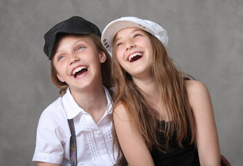 two cute cheerful preteen girls laughing and hugging on grey background