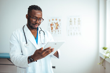 A focused African American male doctor reviews patient information on a digital tablet, wearing a...