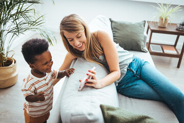 A Caucasian woman and a young African American boy share a moment over a smartphone, highlighting intergenerational tech use in a cozy living room setting.