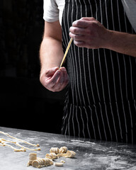 Chef holding freshly prepared pasta in his hands on a dark background