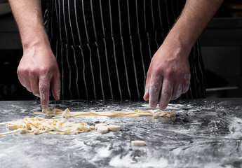 Close-up of the process of making homemade pasta. The chef prepares fresh traditional Italian pasta on a metal table.