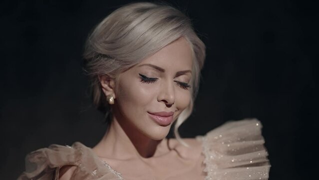 Shy serene and elegant blonde woman closes her eyes gently, wearing a sparkling, beaded evening gown. Her serene expression conveys a sense of peace and beauty.