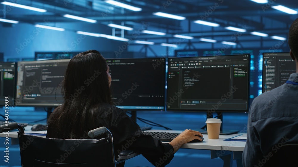 Poster woman with impairment next to diverse coworkers in data center coding on computer. wheelchair user a