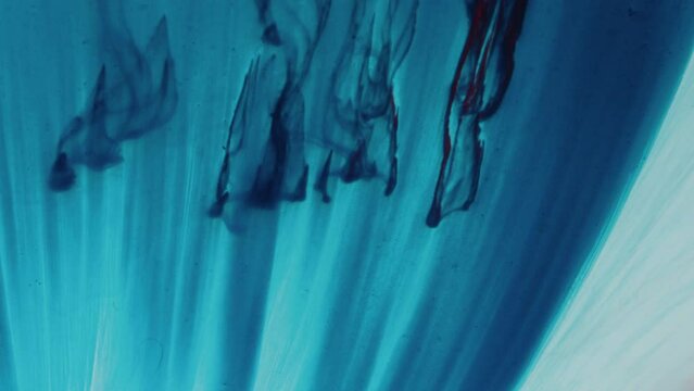 Blue paint drops flowing down in transparent water in slow mo and creating abstract background