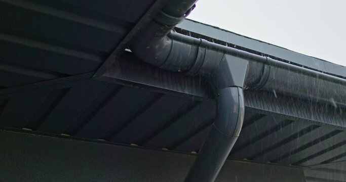 Roof with gutter and downspout under heavy rain.