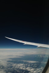 Fototapeta premium A view from the airplane window shows the wing cutting through a sea of fluffy clouds towards a distant blue horizon