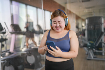 Fototapeta premium Female with smart phone&nbsp;after workout at Gym. Obese asian woman watching online workout training class.