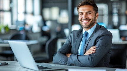 A businessman sits at his desk with a laptop open in front of him, smiling confidently at the camera