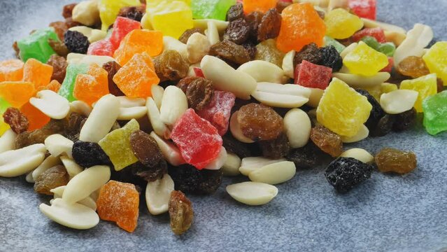 Mix of multi-colored candied fruits and nuts scattered on a gray surface, rotating in a circle. Medium plan
