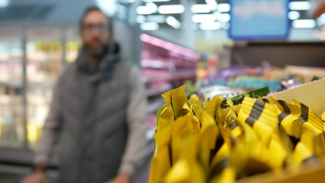 Close-up of many protein bars on the shelf of a supermarket and a male buyer with a shopping trolley takes a few