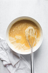 Overhead view of vanilla cake batter being whisked in a white ceramic bowl, flatlay of cake batter being mixed, process of making cake