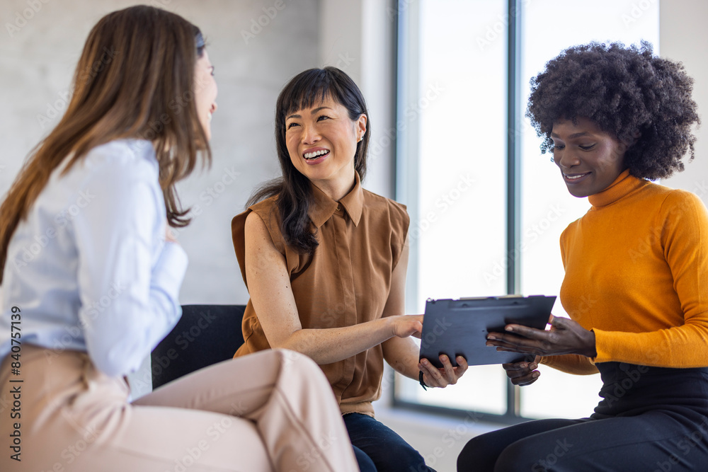 Wall mural three professional women engage in discussion, reviewing data on a clipboard in a bright workspace, 