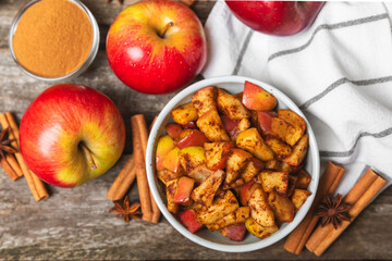 Apples with cinnamon on a textured wooden background. Fragrant red spiced apples with cinnamon sticks and star anise. Apple slices with spicy spices. Place for text. Copy space. Harvesting. Fruits.
