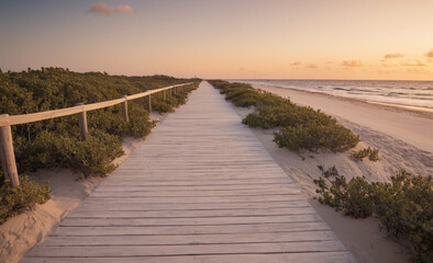 Obraz premium Long Boardwalk to White Sand Beach and Ocean at Sunset with Shrubs on Sides