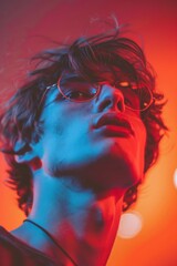 Fototapeta premium Dramatic close-up portrait of young man with curly hair and glasses, illuminated in vibrant red light, capturing thoughtful and intense expression. Intensely lit portrait of young man in red