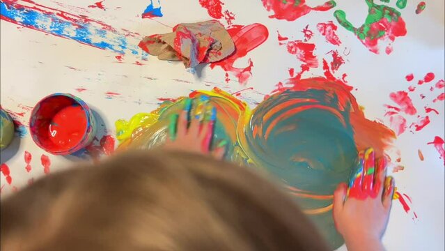 Little cute child with a brush and a palette of paints in his hands draws on a white wall. Happy childhood 