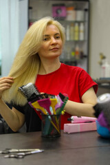 A woman hairdresser in a red T-shirt combs her blond hair in front of a mirror.