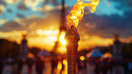 The Olympic torch is in focus and the Eifel Tower on the blurred background during golden hour.