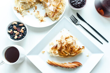 Apple pie with fila dough and sliced apple on a white plate on the table with a cup of tea and nuts. Selected focus.