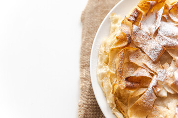 Phyllo pastry pie on a white plate on a table on a light background. Close-up. Copy space.