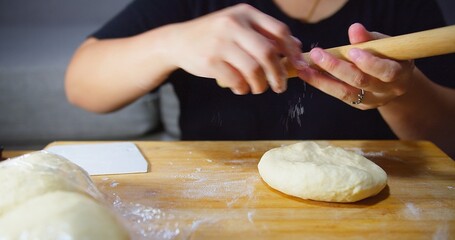 A woman is making a dough on a wooden table. She is holding the dough in her hands and kneading preparing baking bread pizza
