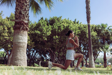 Young and Beautiful Brunette Woman Exercising in the Park on Green Grass, Doing Lunges