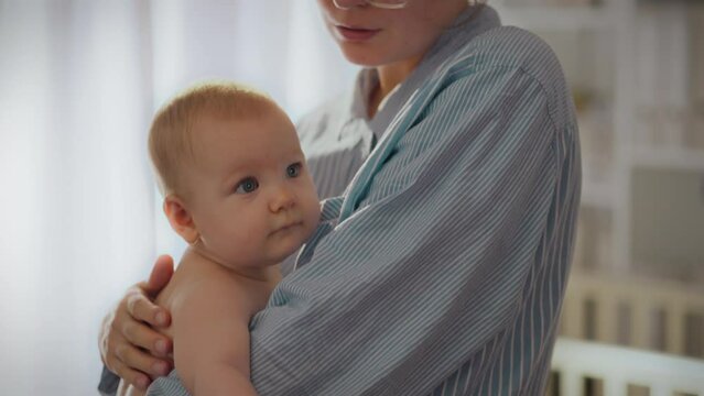 A young mother puts her baby to sleep, gently rocking him in her arms and humming a lullaby. A caring mother calms the baby, putting him to sleep. Young children raising concept