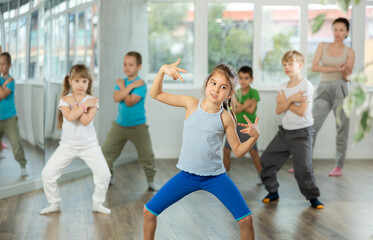 Active preteen girl practicing sport dances with other children and instructor during dancing classes