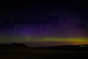 The Northern Lights illuminate the desert night sky, casting a vibrant green and purple glow across the landscape.
