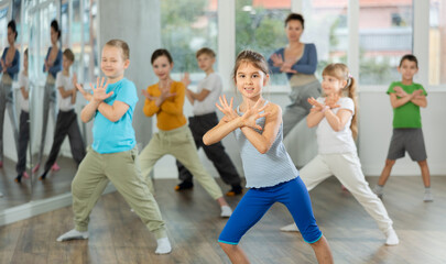 Obraz premium Girl learns to dance hip hop during childrens master class in studio. Teacher watches students, participates in training