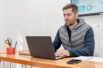 Serious and handsome man working on laptop sitting at his desk.