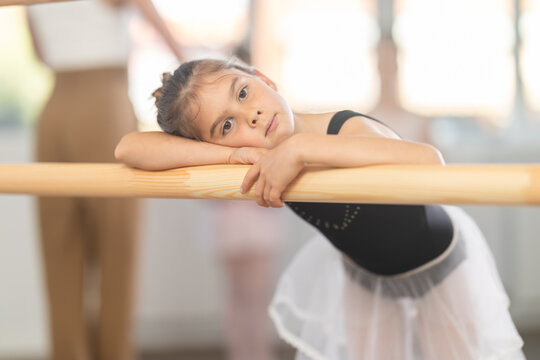 Thoughtful girl stopped her studies, was distracted from her workout, and was resting near ballet machine. Child puts her head on folded hands and dreams and reflects