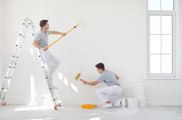Professional team of house painters holding paint rollers and painting the wall of new apartment. Building contractors doing repair renovation preparing to move. Repair and renovating concept. © Studio Romantic