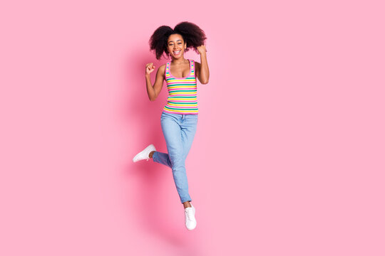 Full size photo of satified woman dressed knit tank denim trousers jumping clenching fists win lottery isolated on pink color background