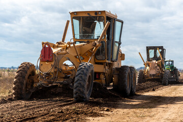 Maquinaria pesada niveladora trabajando en la construcción de una carretera de tierra bajo un...