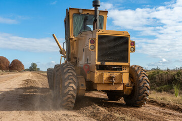 Maquinaria pesada niveladora trabajando en la construcci&oacute;n de una carretera de tierra bajo un cielo despejado