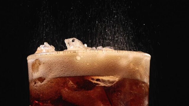Closeup of pouring cola drink with ice cubes. Fizzing cola with ice in glass. Refreshing tasty cola drink.