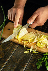 A chef uses a knife in his hand to chop cabbage on a cutting board to prepare borscht for lunch.
