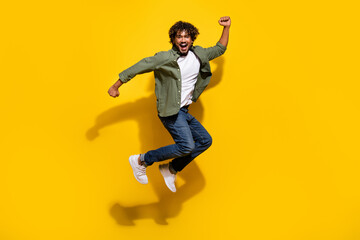Obraz premium Portrait photo of young funny energetic mexican guy in khaki shirt and jeans jumping action isolated on yellow color background