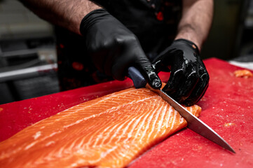 Hands in black gloves expertly slice fresh salmon on a vibrant red cutting board