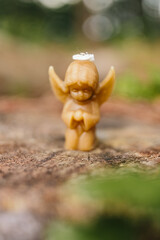 Obraz premium Candle made of natural arganic wax in the shape of a cute angel in nature. A candle on an old stump against the background of a forest. Hobby. Handmade present. Artistic photo of beekeeping products