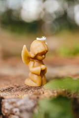 Candle made of natural arganic wax in the shape of a cute angel in nature. A candle on an old stump against the background of a forest. Hobby. Handmade present. Artistic photo of beekeeping products