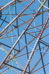 Close up of the metal parts of a Ferris wheel with colorful stripes, with blue and clear sky.