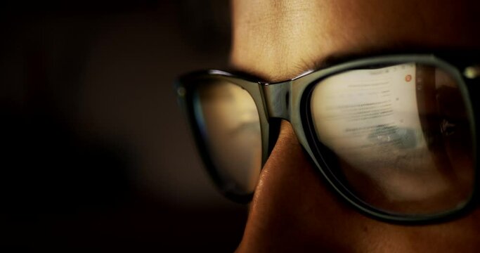 Close-up portrait in profile of part of the face. A young adult Caucasian man wearing glasses whose lenses reflect the reflection of a laptop screen with news on a black background. Fatigue