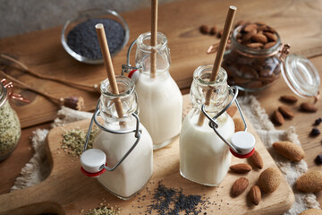 Vegan milks made of hemp seeds, poppy seeds and almonds in three glass bottles with ecological...
