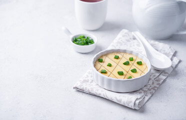 Asian steamed eggs in a bowl with soy sauce and scallions
